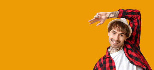 Young tattooed man dancing against orange background with space for text