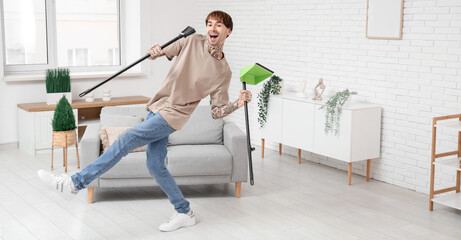Young tattooed man dancing with floor brush and dustpan while cleaning his flat