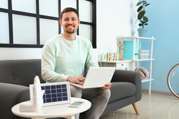 Handsome man using laptop and portable solar panel on table at home