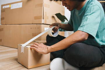 Man sitting on the floor and packing boxes with adhesive tape, indoors. 