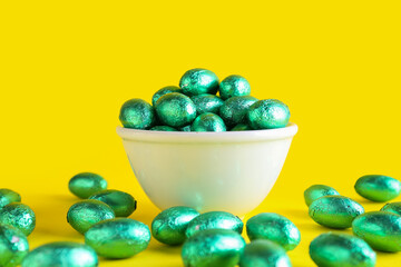 Bowl of chocolate Easter eggs in color foil on yellow background, closeup