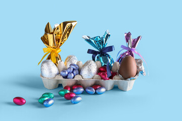 Cardboard holder with chocolate Easter eggs on color background