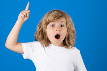 Surprised kid pointing up finger on blue background. Shocked kid pointing to copyspace, showing...