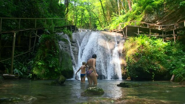 Woman and boy child bathing in beautiful waterfall in dense jungles. Creative. Woman and a boy in cold mountainous river.
