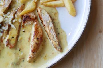 Ready to eat sliced chicken with cream sauce with french fries on a plate .