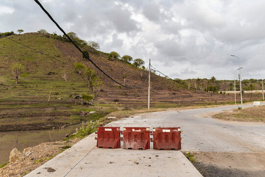 Changing landscape: red construction barriers blocks a rural road with a backdrop of deforested hills and overhead power lines, Indonesia, Asia