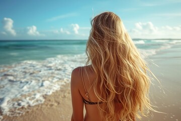Fototapeta na wymiar An attractive young blond woman with beautiful long hair on a sandy beach in the . back view.
