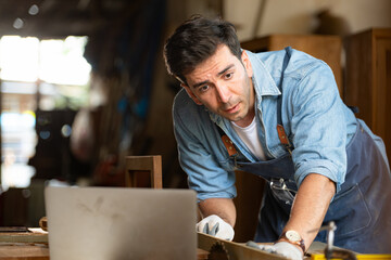 Carpenter working on laptop in his workshop at a woodworking factory