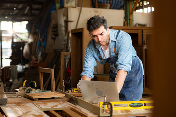 Carpenter working on laptop in his workshop at a woodworking factory