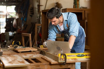 Carpenter working on laptop in his workshop at a woodworking factory