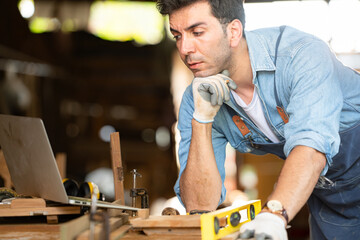 Carpenter working on laptop in his workshop at a woodworking factory