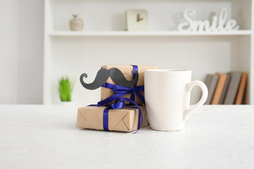 Cup with gifts and paper mustache on table in room. Father's Day celebration