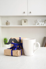 Cup with gifts and paper mustache on table in room. Father's Day celebration