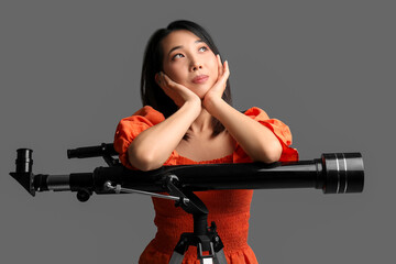 Fototapeta na wymiar Thoughtful young Asian woman with telescope on grey background