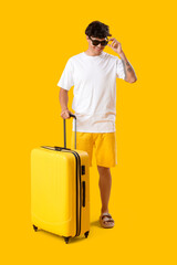 Young man in sunglasses with suitcase on yellow background