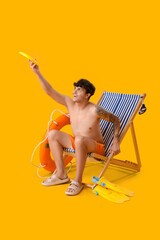 Young man with frisbee disk in deck chair on yellow background
