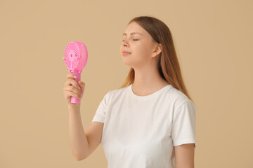 Beautiful young woman with handheld mini fan on beige background