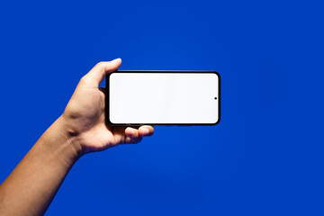 Hand holding smartphone with blank screen on blue green background