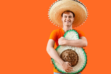 Portrait of young Mexican man in sombrero and with pinata in shape of avocado on orange background