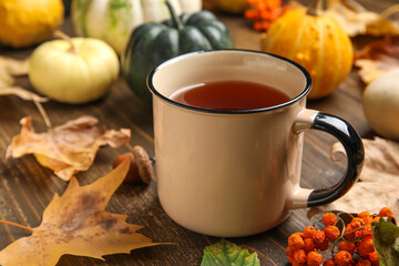 Composition with pumpkins, cup of tea and autumn leaves on brown wooden background