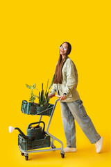 Young woman with plants in cart on yellow background