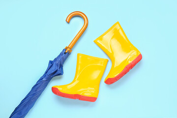 Blue stylish umbrella and gumboots on color background