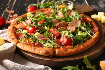 Board of delicious pizza with tomatoes and arugula on black wooden background