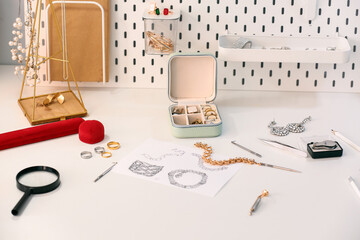 Sketches of stylish accessories with tools on table of jeweler in workshop