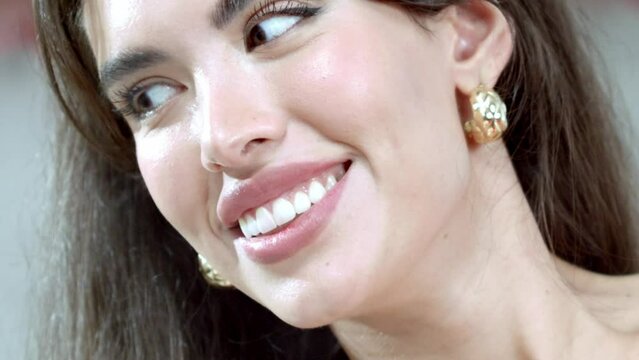 Facial close-up shot of a smiling fashion model wearing gold earrings.