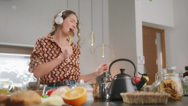 Girl with headphones in kitchen sings along to favorite song using wooden spoon