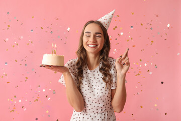 Beautiful young woman in party hat with sweet cake and confetti celebrating Birthday on pink...