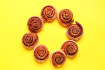 Frame made of tasty cinnamon rolls on yellow background