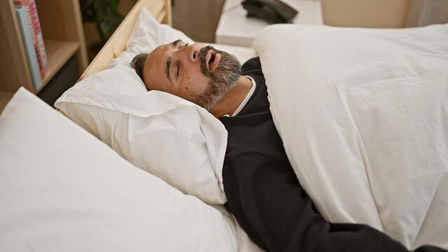 Mature bearded man sleeping peacefully in a cozy bedroom, portraying relaxation and comfort indoors.