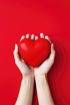Two Hands Holding a Red Heart Against a Red Background