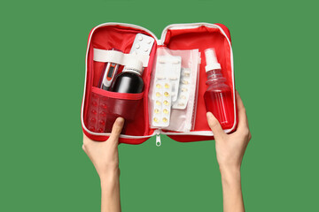 Female hands holding first aid kit with pills and medicine on green background