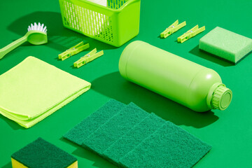 Green cleaning products on a plain green background. Unlabeled detergent bottle, rag, brush and...
