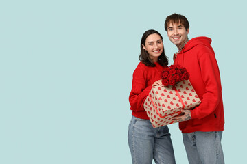 Young couple with bouquet of roses and gift for Valentine's day on blue background