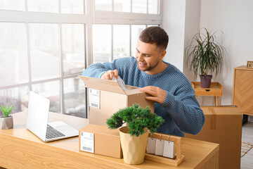 Young man unpacking parcel on table at home