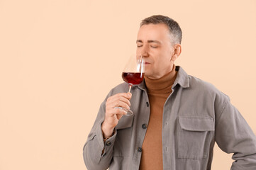 Handsome mature man with glass of wine on beige background
