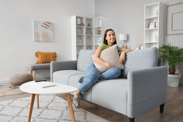 Young woman with cushion sitting on grey sofa in living room