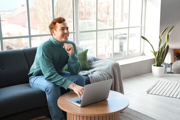 Young man on soft sofa using laptop in living room