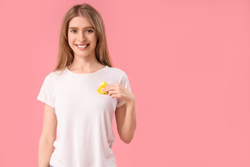 Young woman with yellow awareness ribbon on pink background. World Cancer Day