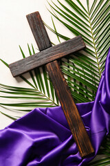 Wooden cross with palm leaves and purple fabric on white background