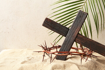 Wooden cross with palm leaf and crown of thorns on sand
