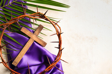 Wooden cross with palm leaf, crown of thorns and purple fabric on white background