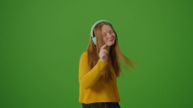Green Screen. Attractive Teenage Girl In Headphones Joyfully Dances. Modern Youth Culture Trends, Popular Platforms And Social Networks. Instagram Stories, TikTok Dances.
