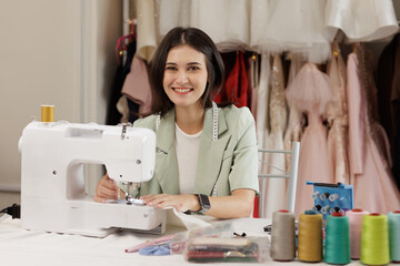  Young woman enjoy work on sewing machine. Fashion designer sewing new wedding dress at workshop....