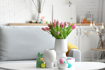Vases with tulips, Easter rabbit and eggs on table in living room