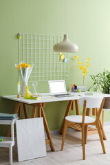 Desk with laptop, tulips in vase, Easter decor and stationery near green wall in room
