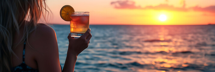 glass with summer juice in womans hand on a background of the sea, refreshing alcohol drink lifestyle
